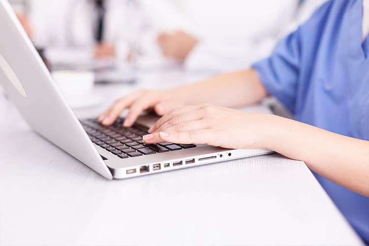 Nurse in scrubs typing on a laptop to complete an online CE course